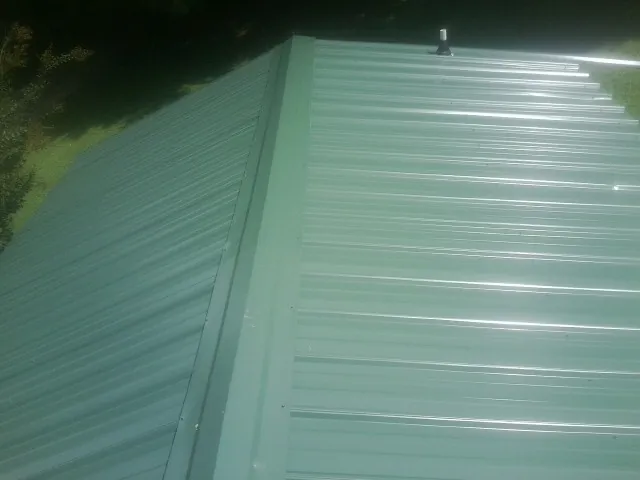 New green metal panels meeting at the ridge of a roof — Flat Roof Repair work by our crew in Bancroft